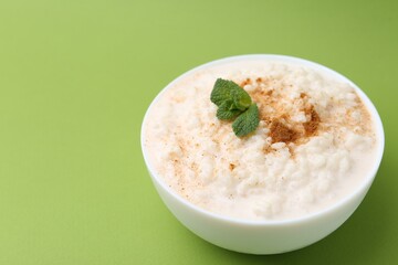 Tasty rice pudding with cinnamon and mint in bowl on green background, closeup. Space for text