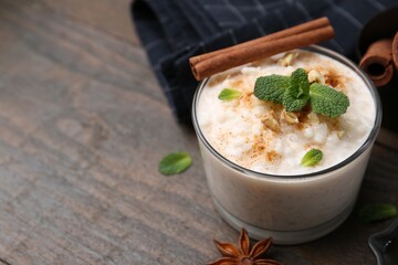 Tasty rice pudding with cinnamon, mint and nuts on wooden table, closeup. Space for text