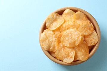 Tasty potato chips in bowl on light blue background, top view. Space for text