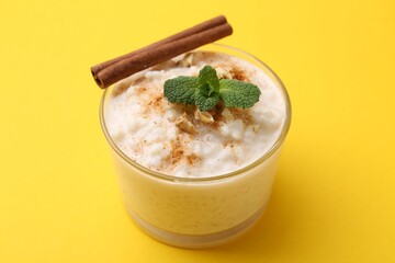 Tasty rice pudding with cinnamon, mint and nuts in glass bowl on yellow background, closeup