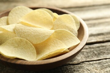 Tasty potato chips in bowl on wooden table, closeup