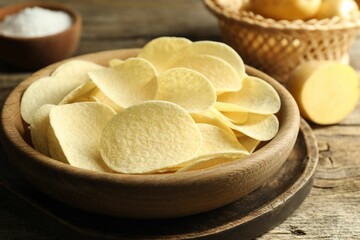 Tasty chips, salt and raw potatoes on wooden table, closeup
