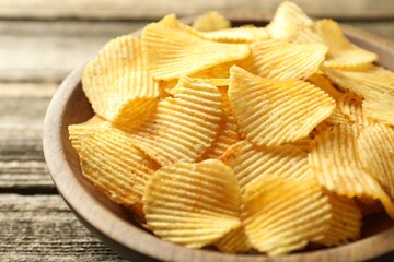 Tasty potato chips in bowl on wooden table, closeup