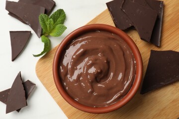 Tasty pudding, mint and pieces of chocolate on white table, flat lay
