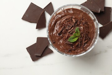 Tasty pudding with mint and pieces of chocolate on white table, flat lay
