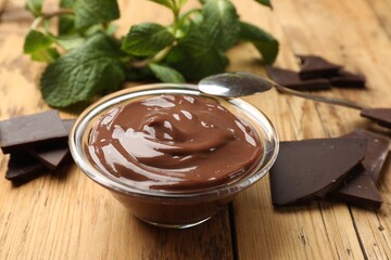 Delicious chocolate mousse in glass bowl and spoon on wooden table, closeup