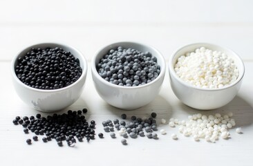 Black, gray and white plastic granules fall out of three round vessels on a white wooden table