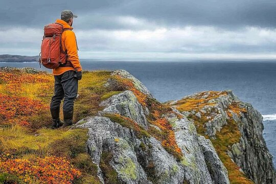 Hiker enjoying a breathtaking coastal view with autumn foliage near the edge of a cliff in a dramatic landscape