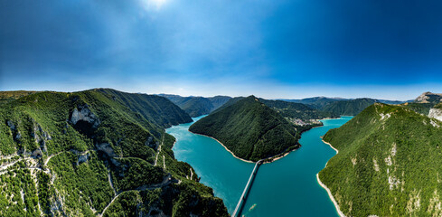 panorama Drone view of a bridge crossing the blue waters of Piva Lake between mountains in Montenegro, near a winding mountain road