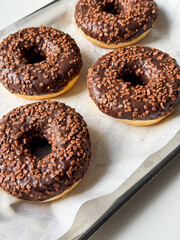 Brown chocolate donuts on metal tray and white table close up