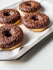 Brown chocolate donuts on metal tray and white table close up