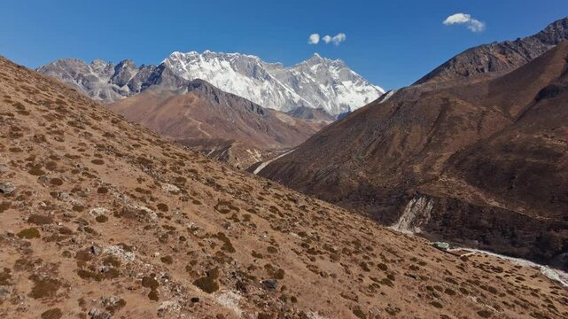 Massive snow capped Everest rising above rocky Himalayan valley, showcasing dramatic geological features of Nepal's legendary mountainous wilderness