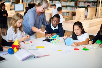 Diverse group of students in a library, engaged in STEM activities. Teacher assists children with educational toys and tablets, fostering learning and creativity. Elementary school children at library
