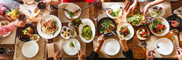 Diverse group dining, sharing food, enjoying a meal. Top view of hands, plates, and drinks....