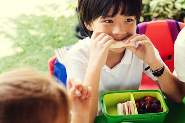 Child eating lunch outdoors, enjoying sandwich and grapes. Lunchtime with packed lunch. Kids having lunch, sharing a meal in a garden. Boy eating sandwich lunch box outdoor. Boy having lunch outdoor