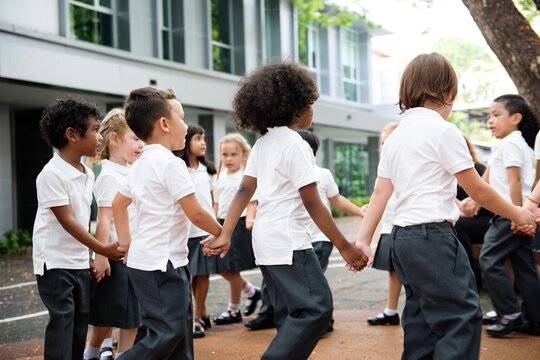 Group of diverse children holding hands in a circle outdoors. Children in school uniforms, playing and smiling. Happy students enjoying playtime together in a outdoor school. Diverse students