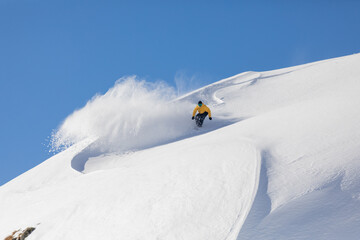 Snowboarder in yellow on pristine snowy slope under clear sky