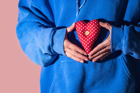 Hands holding a heart shaped pillow in a blue hoodie pocket