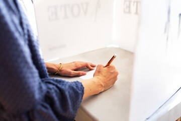 Woman votes in American election, marking her ballot in a voting booth. The woman, engaged in...