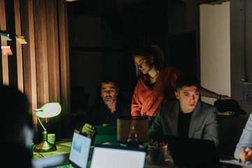 A diverse team of business people working together at night, focusing on finalizing a critical project. The group demonstrates teamwork and determination in a modern office setting.