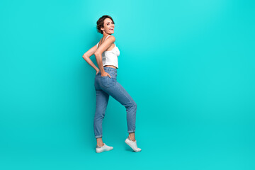 Young woman posing stylishly in casual chic outfit against teal background, looking charismatic and confident