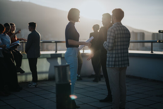 Diverse colleagues gather on a high-rise balcony to brainstorm creative ideas under the setting sun. The scene captures the spirit of teamwork and innovation in a multicultural business environment.