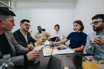 A diverse group of business workers are gathered in a meeting room, analyzing and discussing their project collaboratively. The multicultural team focuses on creative brainstorming and effective