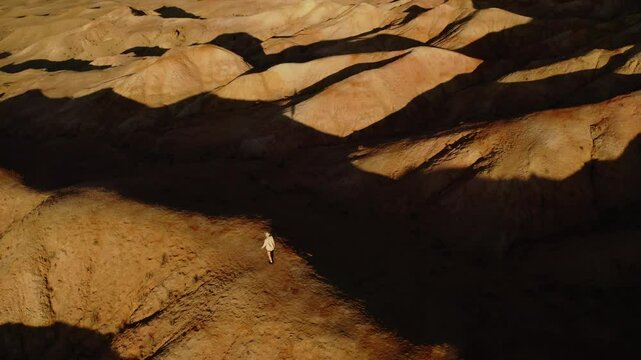 A girl walking through the Mars-like hills of Tsagaan Suvarga, Mongolia, captured in breathtaking aerial drone footage at sunset.