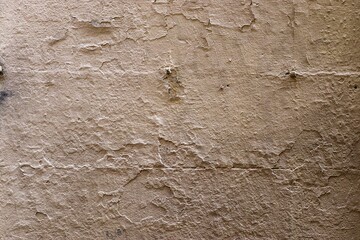 Old beige concrete wall with peeling paint and cracks showing surface imperfections