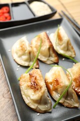 Delicious fried gyoza dumplings with sesame seeds served on wooden table, closeup