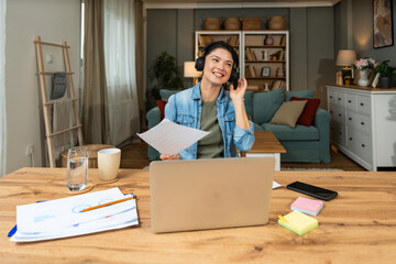 Home office. Young freelance business woman working on laptop, wearing headphones, doing finance....