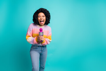 Smiling young woman singing with a microphone, wearing colorful outfit, against a turquoise background