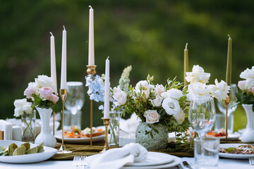 Outdoor dining table features exquisite floral centerpieces and glowing candles. Plates of delicious food are beautifully arranged alongside glassware.
