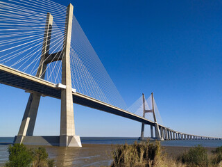 Naklejka premium Stunning cablestayed bridge spanning a vast waterway under a brilliant blue sky. Perfect for projects on infrastructure, travel, engineering, or transportation.