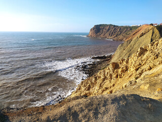 Coastal cliff view of rough waves crashing against the rocks in the afternoon sunlight at a scenic seaside location