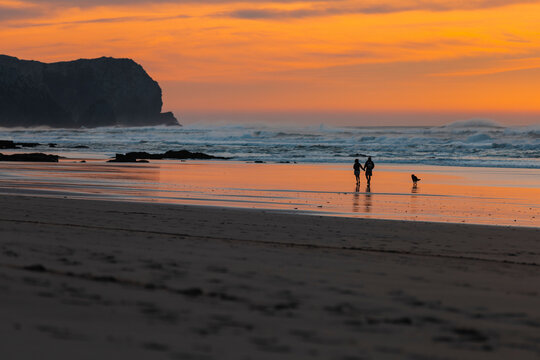 View of a beautiful sunset at the seashore with a couple and a dog, Praia da Cordoama, Sagres, Algarve, Portugal.