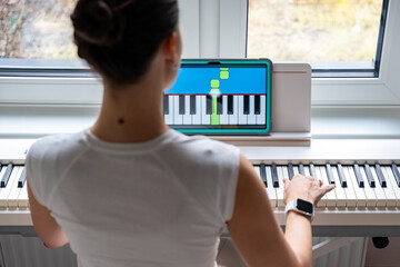 Young woman learning to play the keyboard at home using an interactive app. Using mobile apps for...