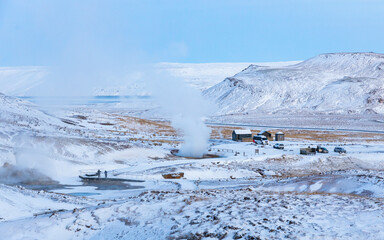 View of hot springs amidst a winter landscape with snow-covered mountains and tourists, Seltun Geothermal Area, Grindavik, Iceland.