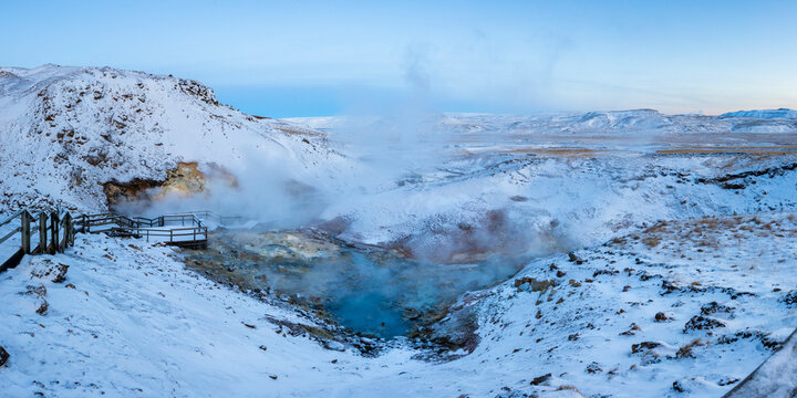 View of hot spring surrounded by snow and steam in winter landscape, Seltun Geothermal Area, Grindavik, Iceland.