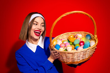 Smiling woman holding a basket of colorful Easter eggs against vibrant red background