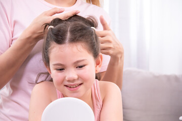 Naklejka premium Mother gently styles daughter hair while girl admires herself in mirror, woman brushes daughter's hair in a peaceful home environment, affectionate bond of parenting, embodies love, and family warmth.
