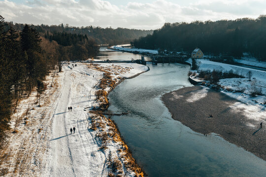 View of isar river with snow-covered forest and tranquil path, Munich, Germany.