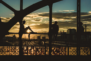 View of Hackerbrucke bridge at sunset with silhouettes of people and railway tracks, Munich, Germany.
