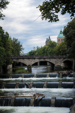 View of St. Lukas Kirche by the serene Isar river with picturesque trees and urban skyline, Munich, Germany.