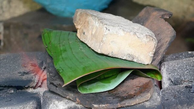 cooking steamed fish covered in banana leaves on a teflon pan. steamed fish in banana leaves with bricks on top
