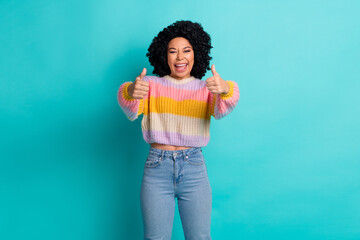 Happy young woman with curly hair giving thumbs-up gesture against turquoise background