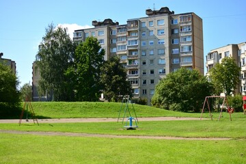 Children playground area near old soviet apartment houses in sunny summer day. Kids swings and play equipment installed in the communal spaces of socialist-era housing estates.