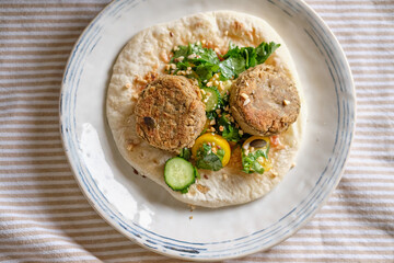 Flatbread with chickpea patty, cherry tomatoes, lettuce, cucumber, cilantro and sesame seeds