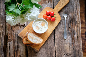 Portion baked eggs with cheese on a board on a wooden table. Flowers, aesthetics.