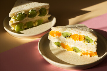 Homemade Korean style bread sandwiches with kiwi, orange, grape and cream cheese on a beige and pink background. Asian dessert. Hard light.